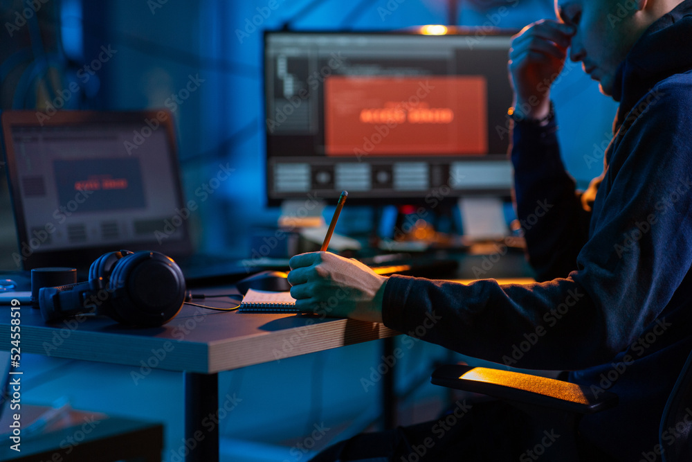 Poster cybercrime, hacking and technology concept - close up of male hacker in dark room writing to noteboo