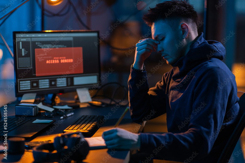 Poster cybercrime, hacking and technology concept - male hacker in dark room writing to notebook and using 