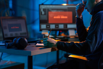 cybercrime, hacking and technology concept - close up of male hacker in dark room writing to...