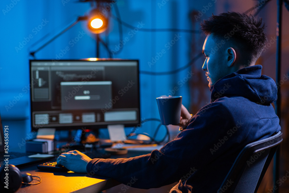 Poster cybercrime, hacking and technology concept - male hacker in dark room drinking coffee and using comp