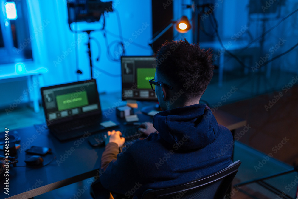 Poster cybercrime, hacking and technology concept - male hacker in dark room writing code or using computer