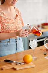 drinks and people concept - close up of woman pouring liquor from glass bottle to jigger and making cocktail at home kitchen