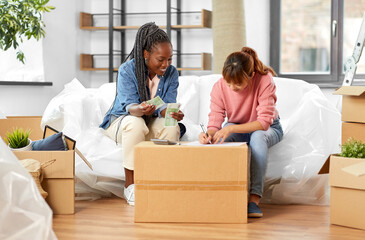 moving, finances and real estate concept - happy smiling women with money, bills and calculator at new home