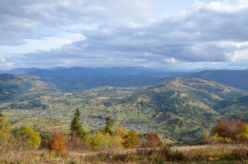 Fototapeta premium Colorful autumn landscape of the mountain village in the valley surrounded by wooded hills. Carpathian mountains, Ukraine