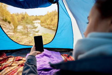 travel, tourism and camping concept - close up of woman with smartphone in sleeping bags in camp...