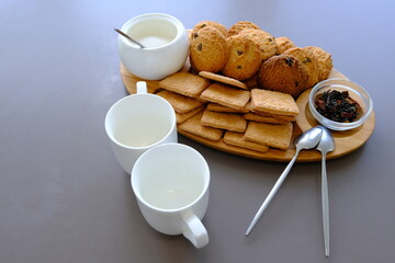 A tasty snack two cups of black tea and a plate of oatmeal cookies a wooden board on the gray background, leaf tea.