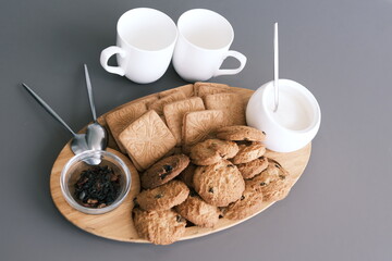 A tasty snack two cups of black tea and a plate of oatmeal cookies a wooden board on the gray background, leaf tea.