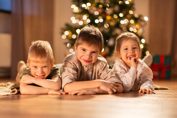 christmas, winter holidays and childhood concept - happy little girl and boys lying on floor at home