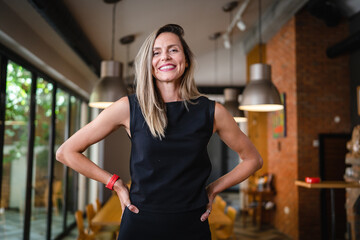 Fototapeta premium One woman middle age caucasian female standing at home in dining room or restaurant happy smile confident wear black waist up copy space front view portrait