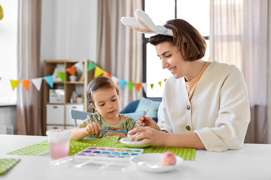 holidays, family and people concept - happy mother and little baby daughter coloring easter eggs with watercolors at home