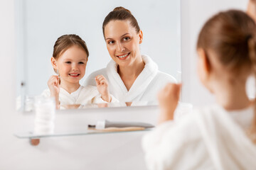 beauty, hygiene, morning and people concept - happy smiling mother and little daughter with dental floss cleaning teeth and looking to mirror at bathroom