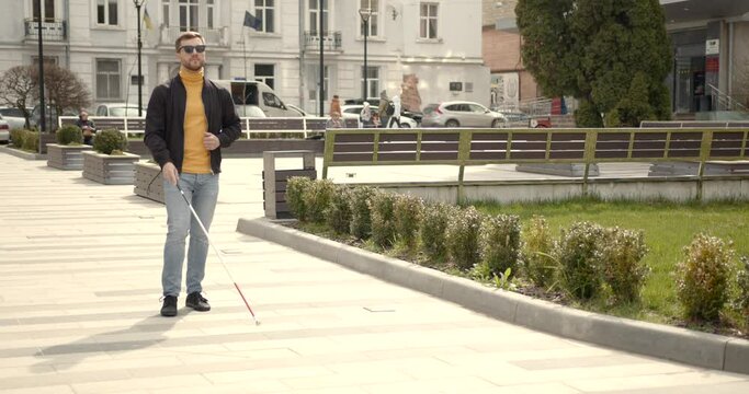 man walking in nature on the side walk holding a stick he is blinded needed directions
