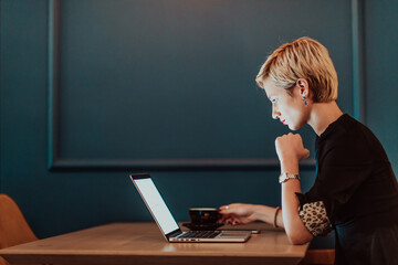 Businesswoman sitting in coffee shop at wooden table, drinking coffee and using laptop. Businesswoman browsing internet, chatting, blogging. Selective focus 