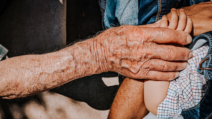 hand of an elderly man holding and stroking a baby's hand,