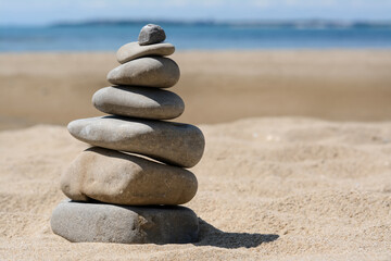 Fototapeta na wymiar Stack of stones on beautiful sandy beach near sea, space for text