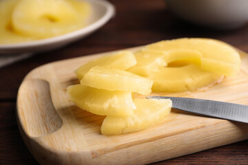 Canned pineapple pieces and knife on wooden board, closeup