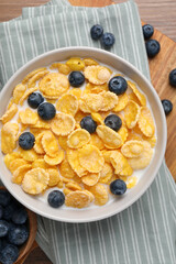 Bowl of tasty crispy corn flakes with milk and blueberries on wooden table, flat lay