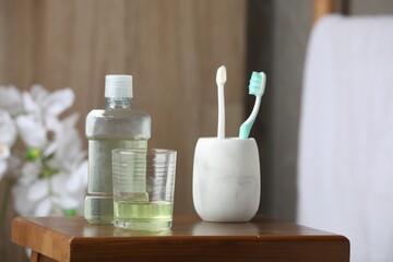 Mouthwash and toothbrushes on wooden table in bathroom