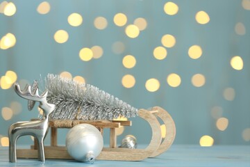 Wooden sleigh with small fir tree near decorative reindeer and Christmas ornament on light blue...