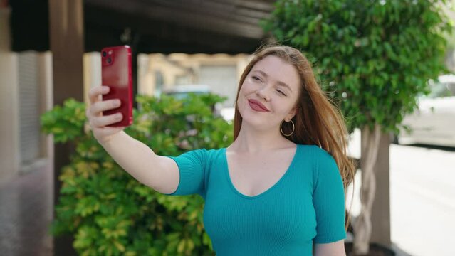 Young redhead woman smiling confident making selfie by the smartphone at street