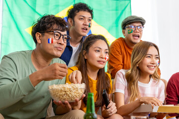 Group of Asian man and woman friends watching soccer games world cup competition on television with eating snack together at home. Sport fans people shouting and celebrating sport team victory match.