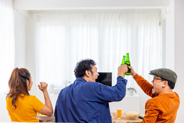 Group of Asian man and woman friends watching soccer games world cup competition on television with...