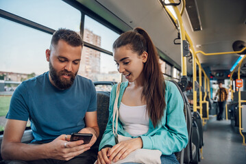 Two friends talking while riding a bus in the city while using a smartphone