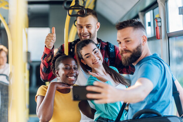 Multiracial group of friends taking selfie with a smartphone in a bus