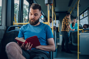 Man is riding in a bus and reading a popular fiction book