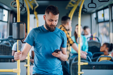 Man is riding in a bus and using a smartphone while holding for a bar