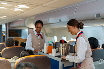  Asian woman flight attendant walking on airplane aisle serving food and drink to passenger in...