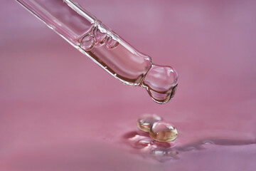 Dropper with serum or cosmetic oil on a pink background.