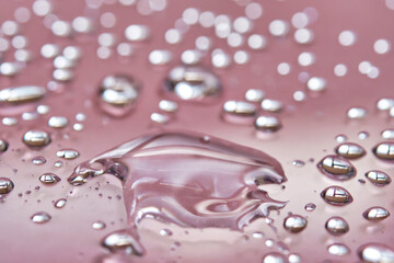 A large drop and splashes of micellar water on a pink background.