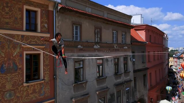 man balances on tight rope, a view of the city from height. Brave Man Slacklining , highlining above people . Nature Adventure and leisure sport . Mountain Balance Extreme Hiker Walking Happy, aerial.