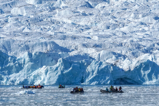 Expedition zodiac boats with tourists exploring the massive calving ice wall of a blue glacier in Disko Bay, Greenland