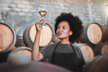 Black woman tasting wine at a winery, looking and checking the color and quality of the years produce. Young African American sommelier proud of the new addition, analyzing white wine in a cellar - Powered by Adobe