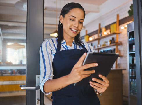 Startup, entrepreneur and female cafe owner working on a digital tablet to plan a budget. Proud, positive and successful leader checking inventory. Small business owner with door open to customers