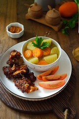 a plate of grilled beef ribs served with vegetables 