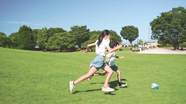 青空の公園でサッカーをするアジア人の子供
