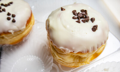 Two delicious donuts with icing sugar and chocolate chips on a white background in a transparent plastic container