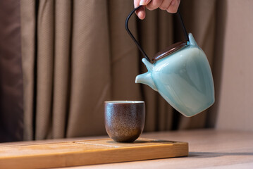 Pouring tea from a teapot into a cup on the table