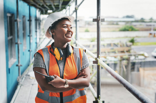 A happy, smiling and cheerful young black woman or senior construction industry worker standing at a building site. A professional female employee working at housing or property development location