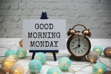 Good Morning Monday text and alarm clock on white brick wall and wooden background