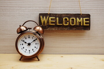 Welcome Sign with alarm clock on wooden background