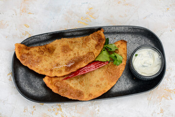 fried chebureks in a black plate with sauce
