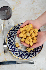 fried pilmeni in hands over a patterned plate on a white background
