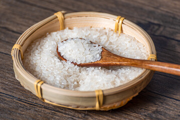 Wooden spoon full of rice in bamboo basket full of rice grains on table