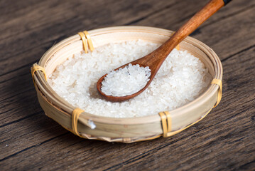 Wooden spoon full of rice in bamboo basket full of rice grains on table