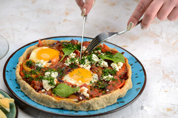 shakshuka in dough in a blue plate on a background with utensils in female hands
