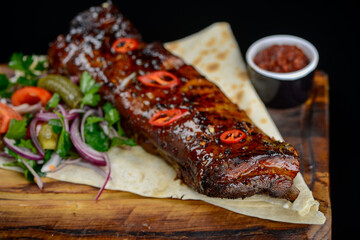 fried ribs on pita bread with salad on a black background macro photo
